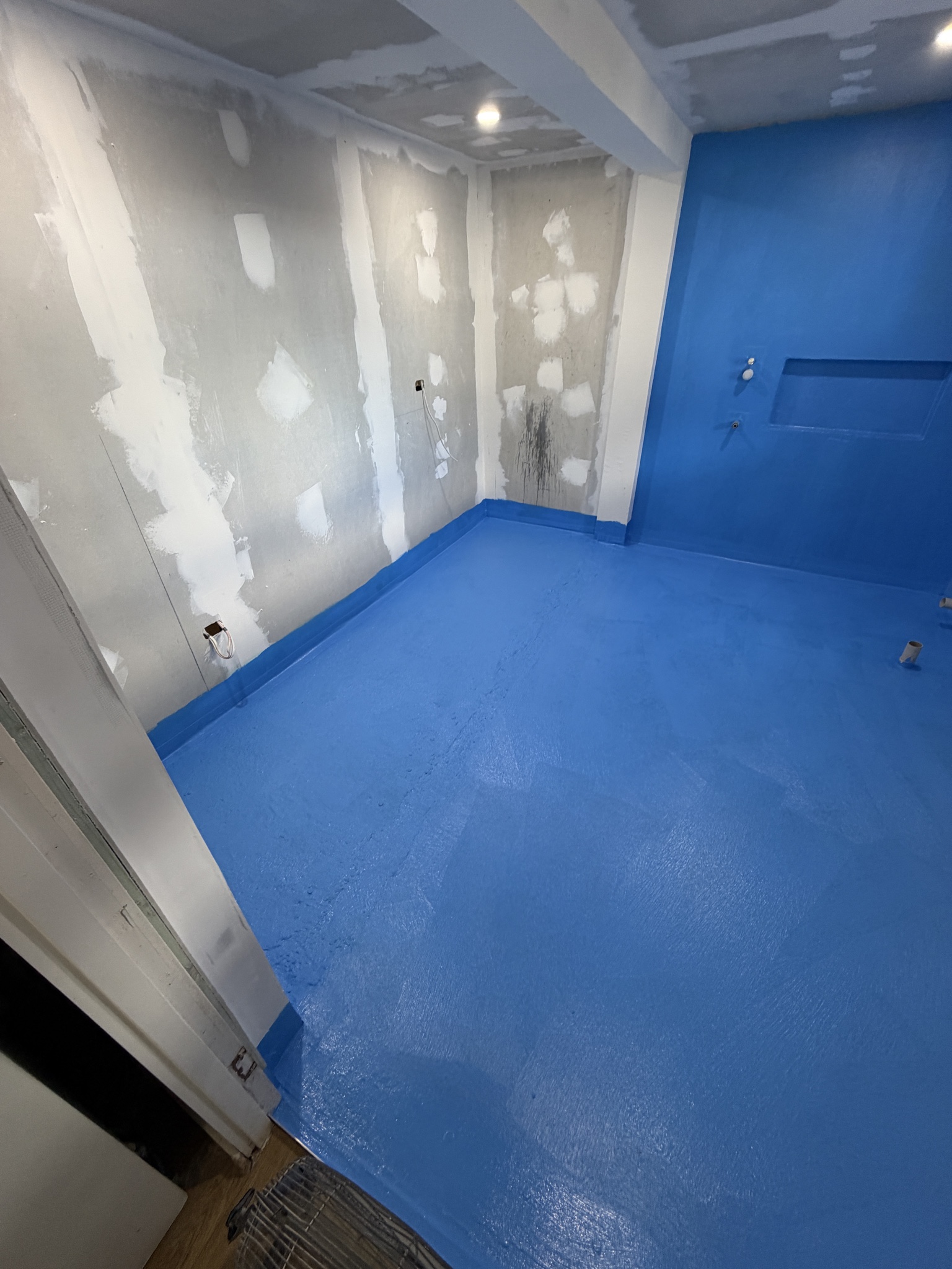 Blue waterproofing membrane applied to a bathroom floor and wall before tiling
