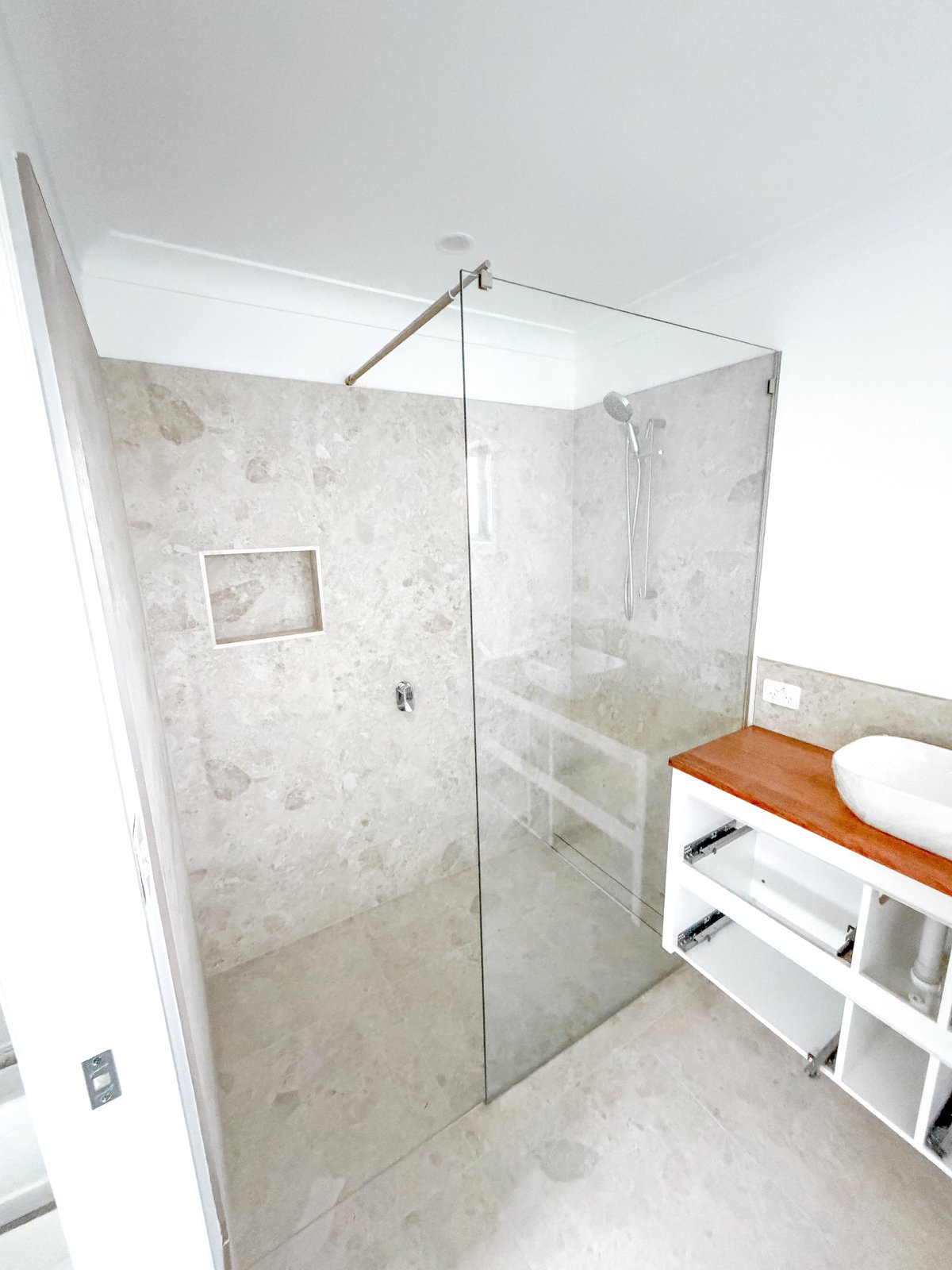 Walk-in shower in cream terrazzo-look tile beside a timber-top vanity