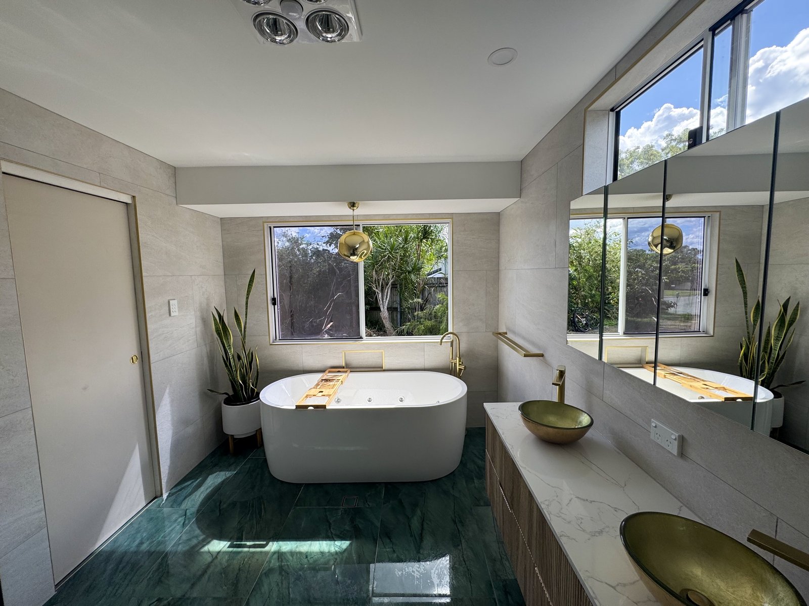 Bathroom with emerald green stone-look floor, freestanding bath and brass tapware