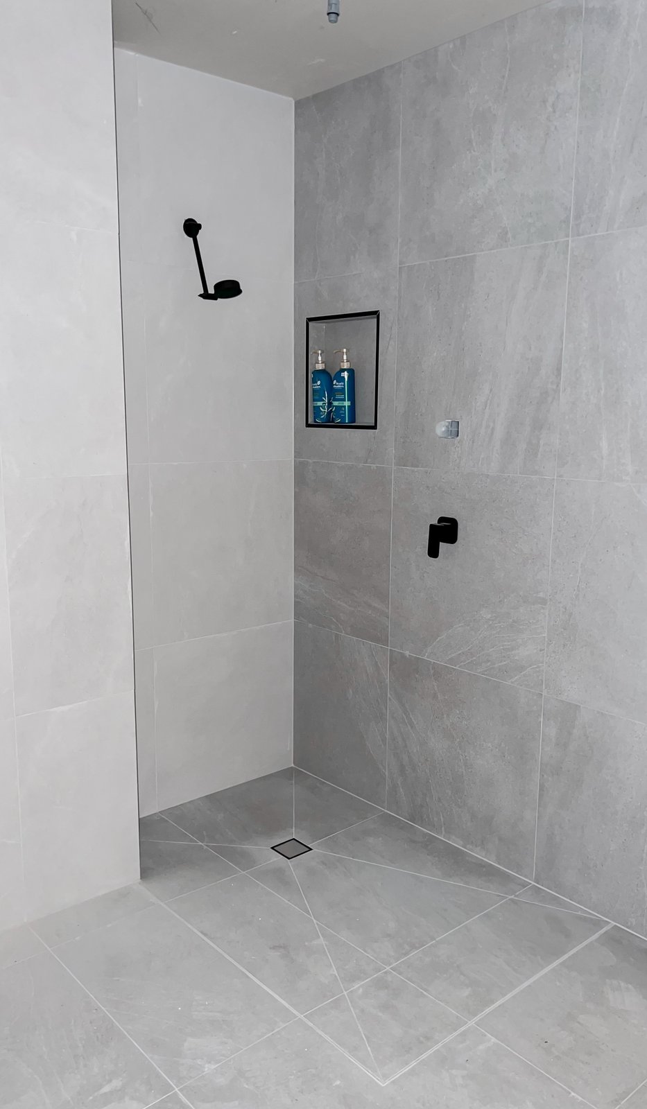 Walk-in shower in large-format grey stone-look tile with matte black tapware