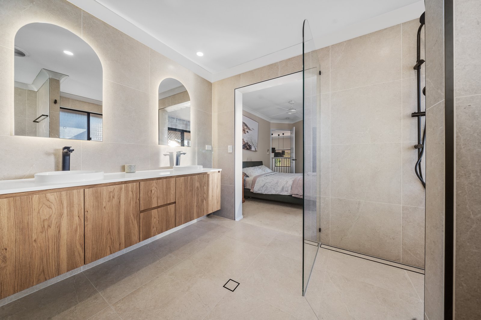 Limestone-look bathroom with floating timber double vanity and backlit arch mirrors