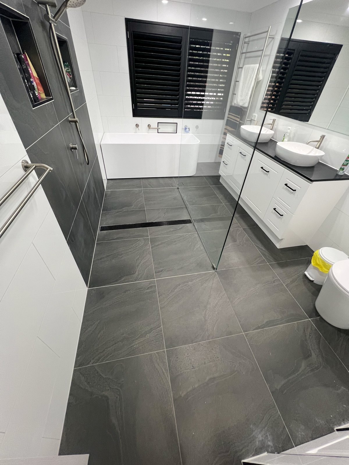 White bathroom with charcoal slate-look floor, freestanding bath and double vanity