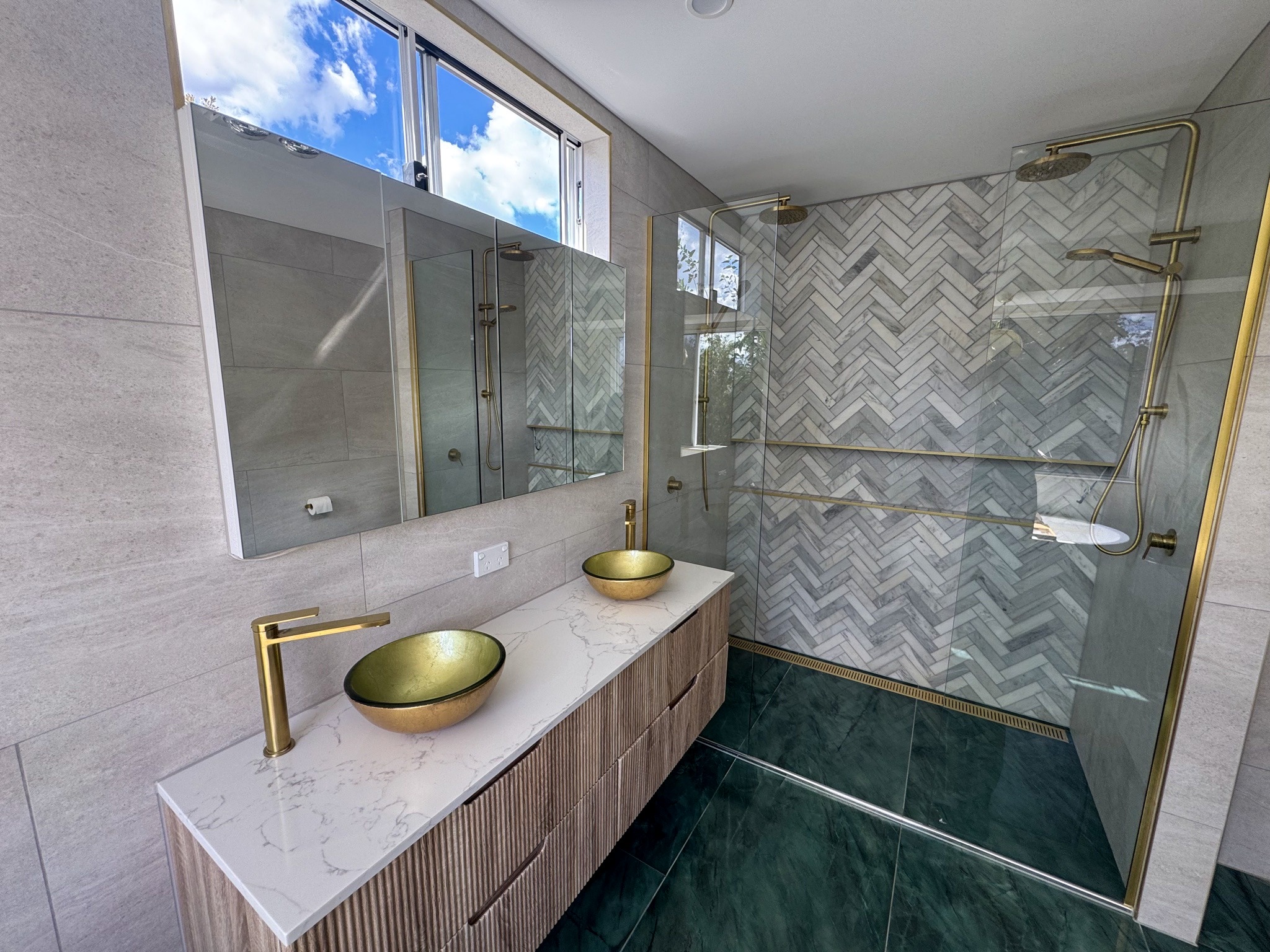 Gold vessel basins on the fluted timber vanity with the herringbone shower behind