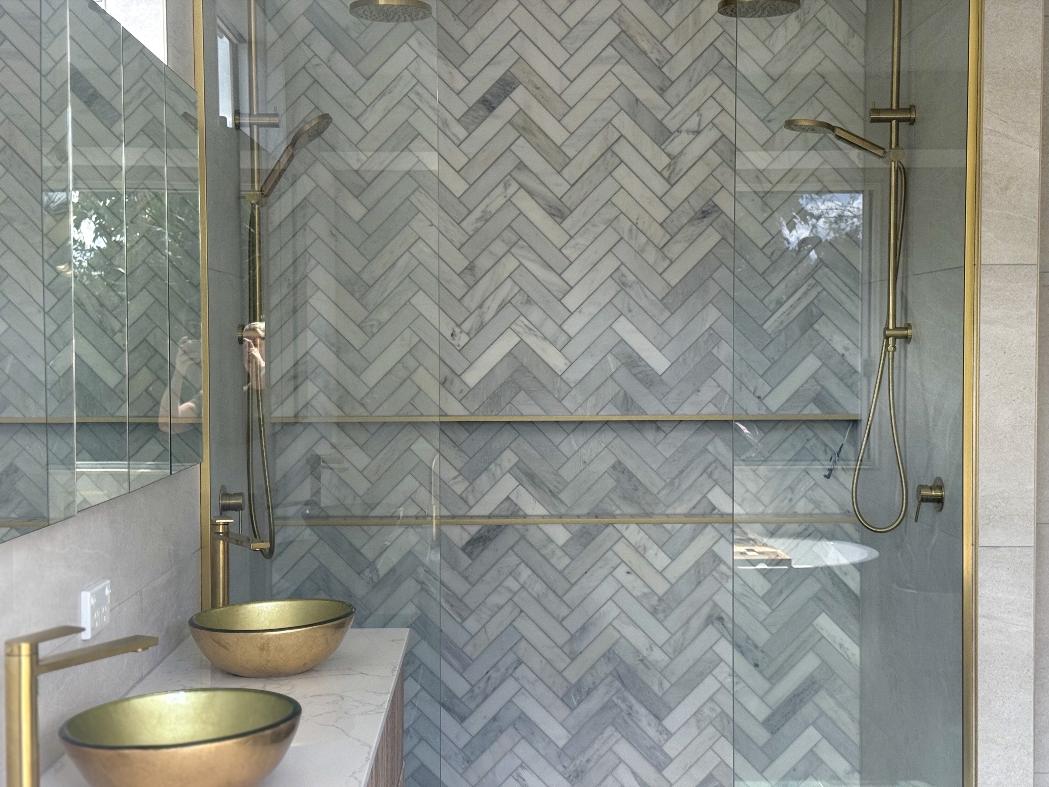 Marble herringbone shower with brass rails and twin shower heads