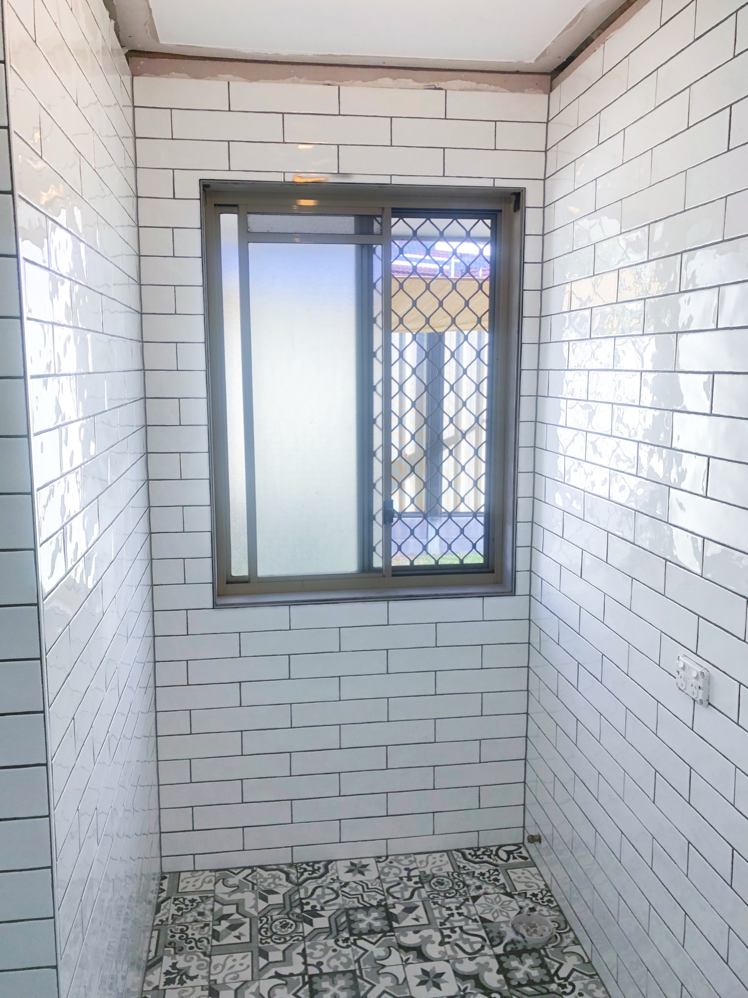 White subway walls above the patterned heritage-look floor, tiling complete